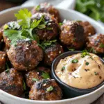 A plate of juicy Korean BBQ meatballs garnished with fresh cilantro and sesame seeds, served with a creamy spicy mayo dip in a small bowl.