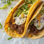 Two delicious smash burger tacos with crispy beef patties, shredded lettuce, creamy sauce, and melted cheese in lightly charred corn tortillas.