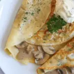 Delicate crepes filled with creamy chicken and mushroom sauce, garnished with fresh herbs and served with a dollop of herb-infused sour cream.