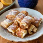 A plate of lovely Cinnamon Roll French Toast Roll-Ups, filled with creamy filling, dusted with powdered sugar, and drizzled with syrup.