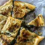 Golden, crispy Spanakopita Pan Pittes cut into squares, revealing a delicious spinach and feta filling.