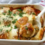 A baked dish filled with meatballs, toasted bread, marinara sauce, and melted cheese, garnished with fresh parsley and Parmesan.