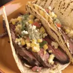 Grilled steak elote tacos with tender sliced steak, charred corn, crumbled cheese, and fresh salsa, served on warm, grilled tortillas.