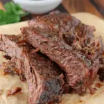 Tender, fall-apart Texas-style boneless beef ribs served on parchment paper with barbecue sauce in the background.