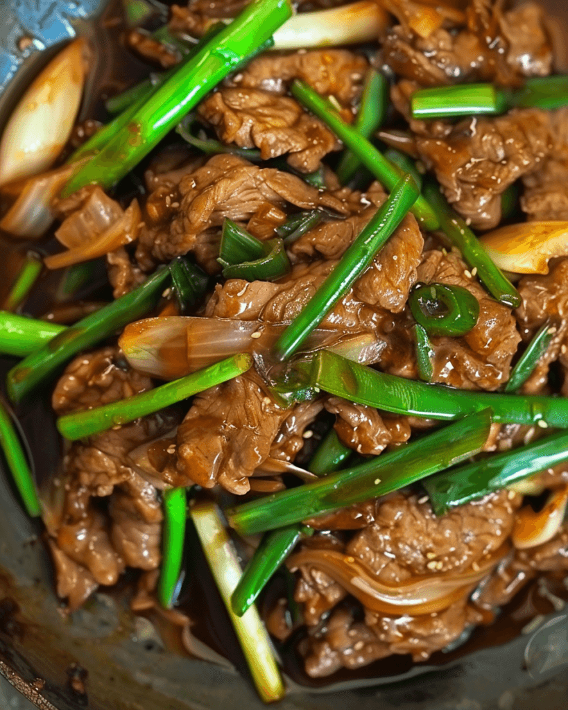 A close-up of Spicy Scallion Beef Stir-fry with tender beef slices, crisp scallions, and onions coated in a rich, savory sauce.