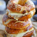 Stack of warm pretzel sandwiches with sesame seeds and melted Swiss cheese oozing between layers
