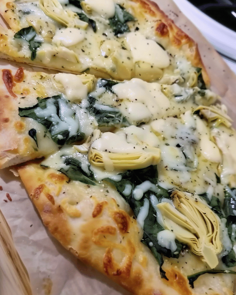 Baked flatbread pizza topped with melted cheese, fresh spinach, and marinated artichoke hearts on a golden crust.