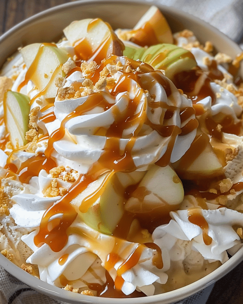 Close-up of a caramel apple fluff salad topped with whipped cream, green apple slices, caramel drizzle, and crushed cookies.