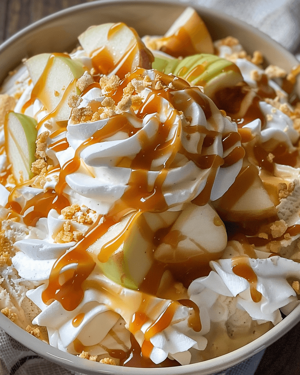 Close-up of a caramel apple fluff salad topped with whipped cream, green apple slices, caramel drizzle, and crushed cookies.