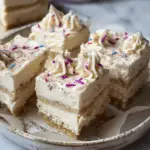 Close-up of festive sugar cookie cheesecake bars with colorful sprinkles and piped whipped cream on top, resting on a decorative plate.
