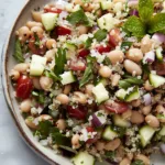 A fresh quinoa and cannellini bean salad with chopped cucumber, cherry tomatoes, red onion, parsley, and mint served in a rustic bowl.