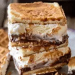 Stack of s’mores ice cream sandwiches made with graham crackers, layers of chocolate, and creamy vanilla ice cream, slightly melting.
