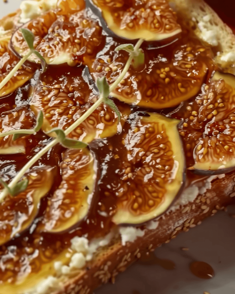 Close-up of a slice of sesame seed bread topped with creamy cottage cheese, fresh fig slices, glossy fig jam, and a sprig of fresh thyme.