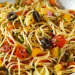 Bowl of cold spaghetti salad mixed with chopped tomatoes, bell peppers, black olives, zucchini, and herbs, lightly dressed with vinaigrette and black pepper.