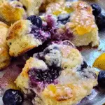 Fluffy lemon blueberry biscuits topped with melted butter and glaze, surrounded by fresh blueberries and lemon slices.