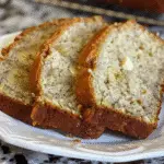 Three slices of moist banana bread with visible banana pieces, served on a white plate over a marbled countertop.