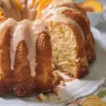 Close-up of a sliced peach buttermilk pound cake with vanilla glaze, garnished with fresh peach slices.