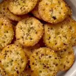 Golden Ritz Bits crackers coated in garlic butter and herbs, sprinkled with sesame seeds and seasonings in a white serving bowl.