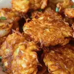 Close-up of crispy golden Amish onion fritters in a white bowl, garnished with chopped green onions.