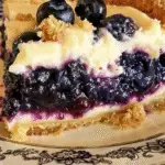 Close-up of a slice of blueberry cream cheese crumb bar with a golden crust, creamy filling, juicy blueberries, and crumb topping.
