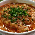Bowl of cabbage roll soup with chopped green herbs on top, featuring a tomato-based broth with ground meat and cooked cabbage.