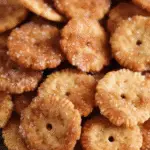 A close-up of golden Ritz crackers coated in cinnamon sugar, stacked in a decorative glass dish.