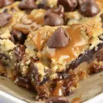 Close-up of a gooey coconut toffee chocolate chip cookie bar topped with melted caramel and chocolate chips in a baking dish.