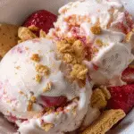 Scoops of creamy cottage cheese ice cream with swirls of strawberry, topped with crumbled graham crackers and fresh strawberries in a white bowl.