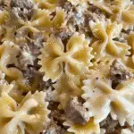 Close-up of creamy bowtie pasta with ground beef and a Parmesan garlic sauce, garnished with a light sprinkle of cheese and black pepper.