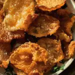 A bowl of golden, crispy fried pickle chips sprinkled with coarse salt and garnished with parsley.