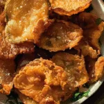 A bowl of golden, crispy fried pickle chips sprinkled with coarse salt and garnished with parsley.