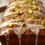 Close-up of a loaf of lemon pistachio bread topped with white glaze and chopped pistachios.