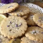 Stack of round lemon lavender cookies topped with coarse sugar and lavender buds, garnished with lemon slices and fresh lavender flowers