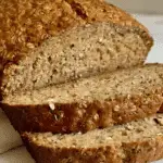 Close-up of sliced flourless oat and chia seed bread with a golden crust and a hearty, textured crumb.