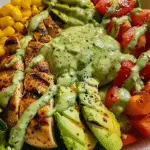 Colorful grilled chicken salad bowl with sliced avocado, cherry tomatoes, corn, and creamy green dressing over fresh greens.