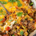 Close-up of a hearty layered taco casserole with ground beef, melted cheese, black beans, corn, and diced vegetables, topped with fresh cilantro.
