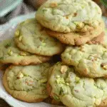 A plate stacked with soft, green pistachio pudding cookies studded with chopped pistachios.