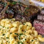 Close-up of creamy Cajun Alfredo macaroni pasta served with juicy garlic butter steak bites, garnished with chopped herbs.