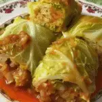 Stuffed cabbage rolls filled with rice and vegetables, served in tomato sauce on a decorative floral plate.