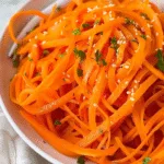Julienned carrot salad with chopped parsley and sesame seeds in a white bowl on a light cloth background.