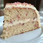 Slice of Southern pecan butter cake with creamy frosting and pink sprinkles on a white plate.