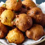 A close-up of freshly fried hush puppies piled in a bowl lined with paper towels, showing a crispy golden-brown crust.