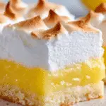 Close-up of a lemon meringue pie bar with a buttery shortbread crust, bright lemon curd filling, and golden toasted meringue topping.